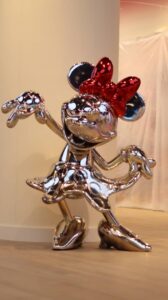 Metallic Minnie Mouse sculpture with a red bow, showcasing a playful pose and shiny surface, ideal for collectors and Disney fans.